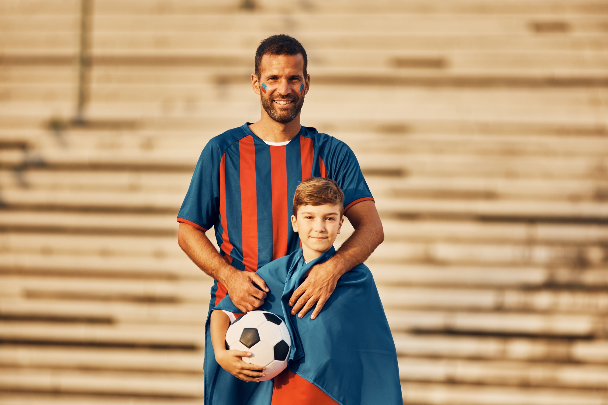 Portrait of happy father and son in soccer jerseys looking at camera.